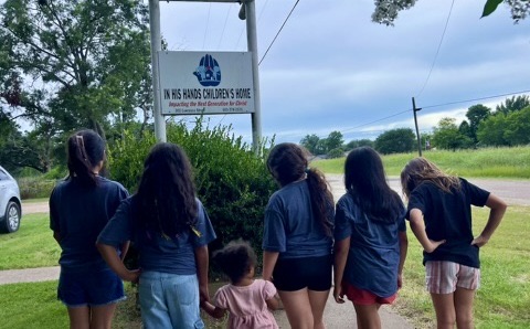 Girls from the home standing together in front of the In His Hands sign.