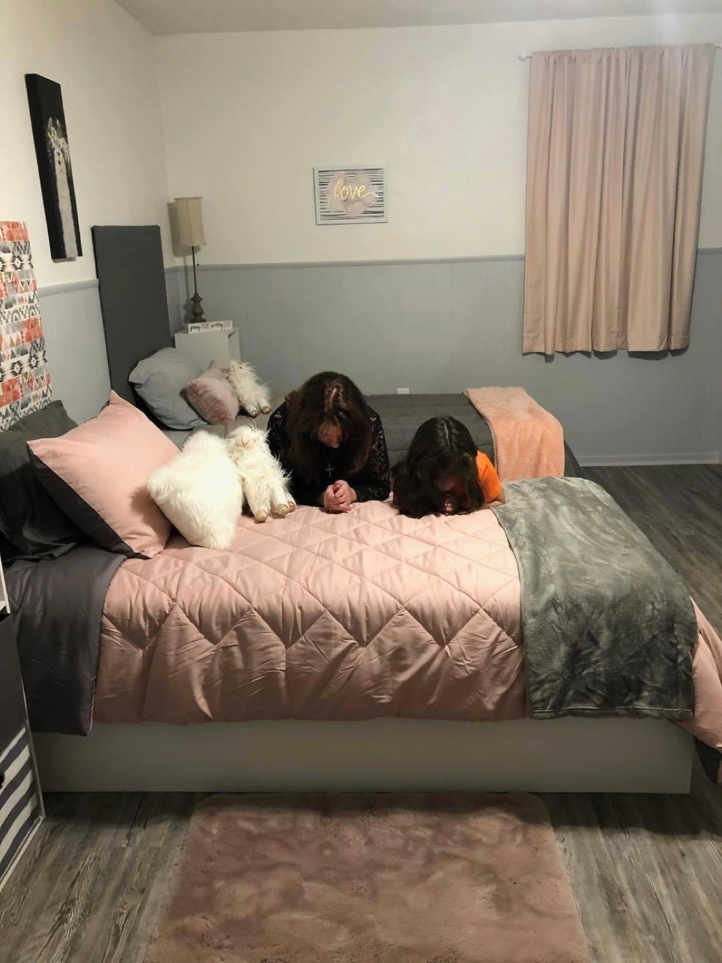 A house parent and a child praying together beside a bed.