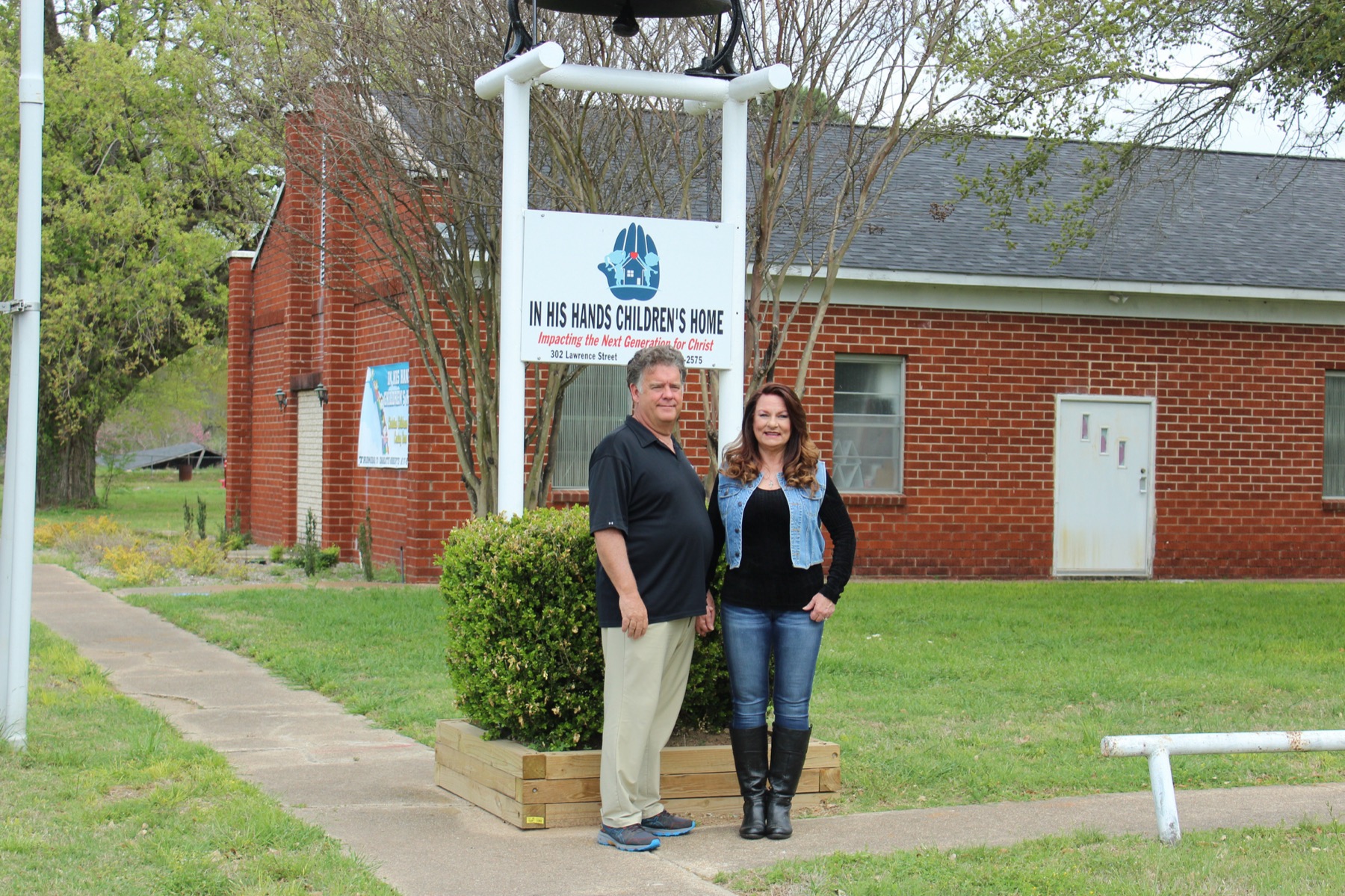 Hugh and Charlotte Roberts beside the In His Hands Children's Home sign in front of the brick home.