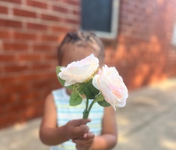 A child holding white roses in front of the brick home.