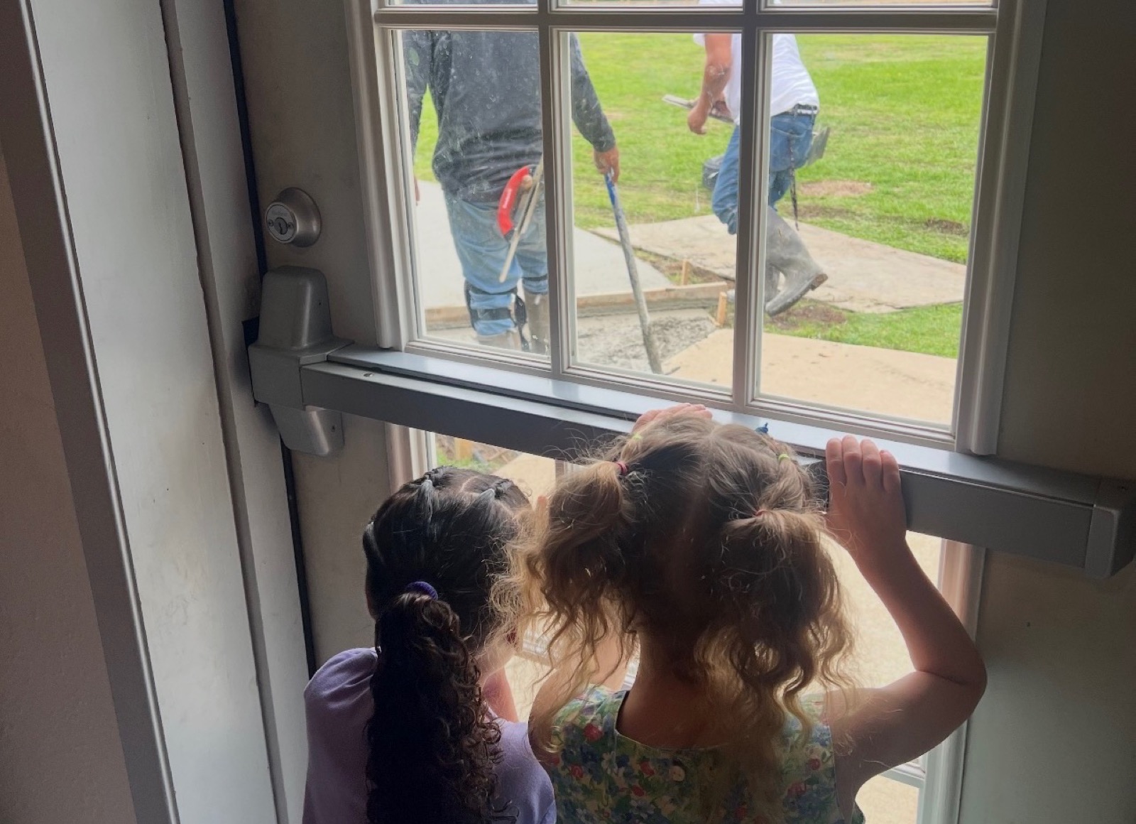 Two girls looking out a window while work is done outside the home.